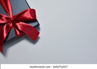 Black gift box with silk red ribbon bow on neutral paper background. Christmas present, valentine day, birthday concept. Flat lay, top view. Vertical position 