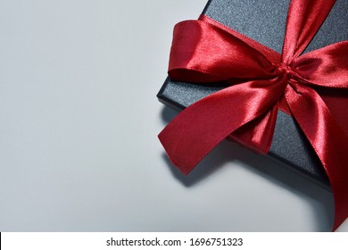 Black gift box with silk red ribbon bow on neutral paper background. Christmas present, valentine day, birthday concept. Flat lay, top view.