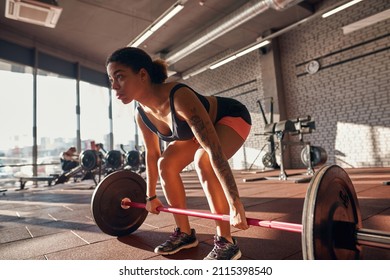 Black girl doing deadlift exercise with barbell for back in gym. Concept of healthy lifestyle. Young focused curly brunette woman wearing sportswear. Fitness center in sunny day - Powered by Shutterstock