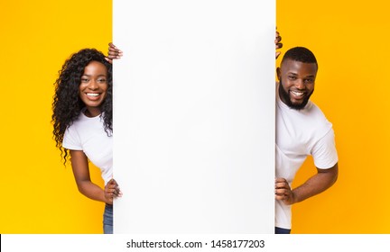 Black Girl And Guy Holding White Advertising Board, yellow studio background, panorama - Shutterstock ID 1458177203