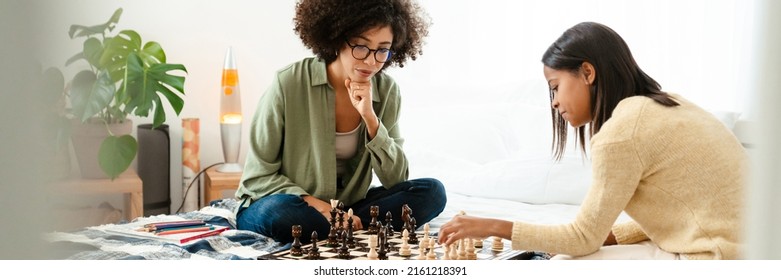 Black girl and her mother playing chess together on bed at home - Powered by Shutterstock