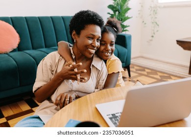 Black girl and her mother share a loving moment at home, sitting together in the living room and watching a movie on a laptop. Young daughter wrapping her arms around her mom during movie time. - Powered by Shutterstock