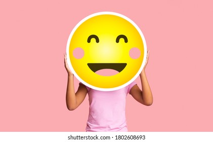 Black Girl Hiding Face Behind Happy Shy Emoji Emoticon, Standing Over Pink Studio Background With Copy Space