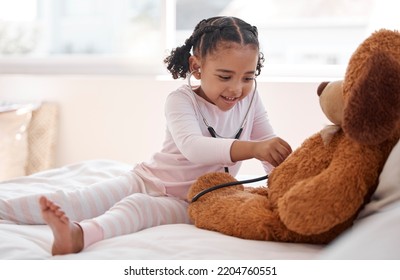 A Black Girl Playing Hospital Doctor With A Teddy Bear On Her Bed, Holding A Stethoscope And Imagining A Kid. Child Development For A Future Job As A Physician, Clinic Nurse And Medical Professional