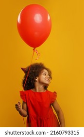 A Black Girl In A Red Birthday Hat On Her Head And A Red Dress, With A Red Balloon In Her Hand In Anticipation Of The Holiday And Emotions.