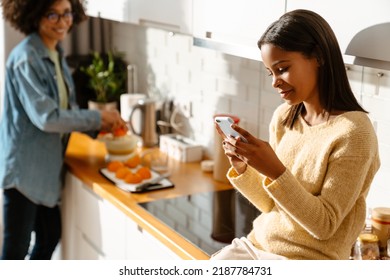 Black Girl Using Mobile Phone During Spending Time With Her Mother In Kitchen At Home