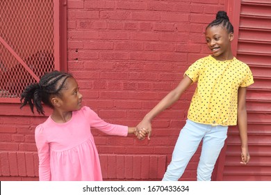 Black Girls Wearing Bright Colors  Holding Hands In Front Of Red Brick Background