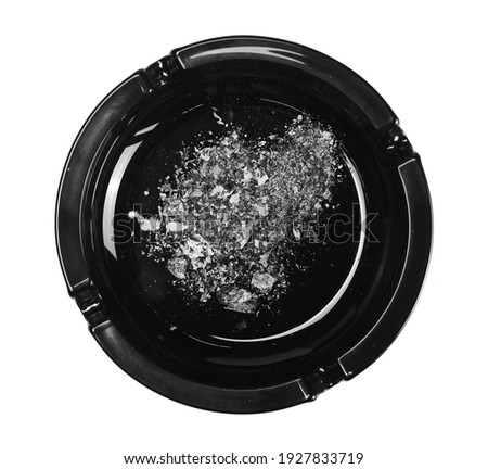 Black glass ashtray with cigarette stubs, butts with ash isolated on white background, top view