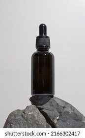 Black glass dropper bottle with a pipette on stones, grey background. Natural cosmetics concept, natural essential oil.