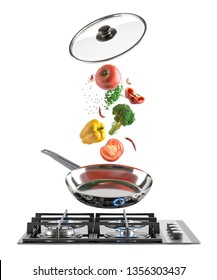 Black Glass gas cooking plate and chrome frying pan with flying colorful fresh vegetables and glass lid. White isolated background.