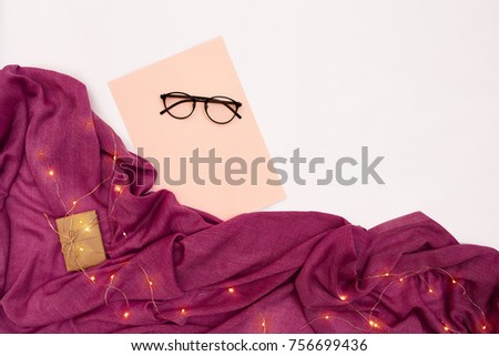 Black glasses, pink paper with new years goals. Scarf and Christmas lights on white background.