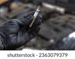 A black gloved hand holding a car spark plug. Vehicle maintenance concept.