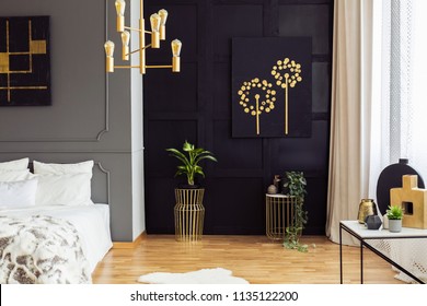 Black And Gold Poster Above Plants In Bedroom Interior With White Pillows On Bed. Real Photo