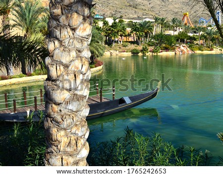 Black gondola tied near wooden dock on lake in tropic amusement park. Spain, Benidorm, Terra Mitica park.