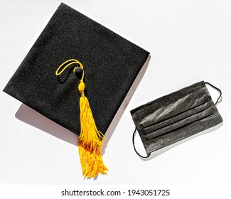 Black graduate cap with yellow tassel and protective face mask on white background, protection from virus while studying, getting diploma in new reality, new normal, Flat lay, top view, mortarboard