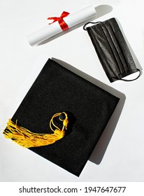 Black graduate cap yellow tassel, paper scroll with red ribbon bow, protective face mask on white background, protection from virus, getting diploma in new reality, new normal, top view, mortarboard