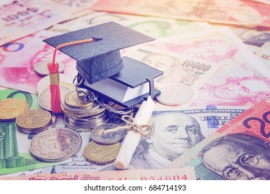 Black graduation cap / hat, a rolled up scroll diploma / certificate and a tiny or small book on pile of coin and banknotes. Concept of international graduate program or graduate study abroad program.