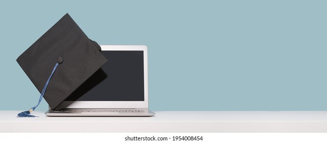 Black Graduation Cap over a laptop. Masters or Bachelors Degree thesis writing. Knowledge online courses qualifications and higher education with copy space. Lockdown. banner. Distant learning - Shutterstock ID 1954008454