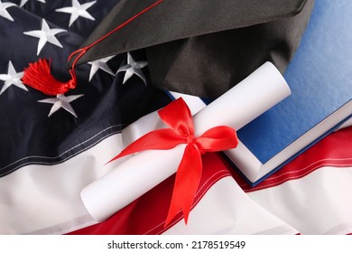 Black graduation hat, diploma and book on American flag, above view