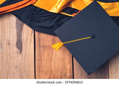 Black Graduation Hat And Graduation Gown Placed On Old Wood Background