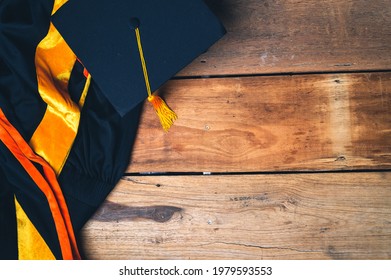 Black Graduation Hat And Graduation Gown Placed On Old Wood Background