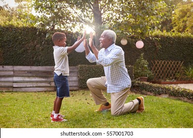 Black grandfather plays with grandson in garden, full length