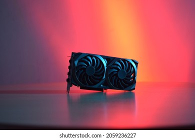 Black graphics card with two fans, on a wooden table, with red and blue lighting.