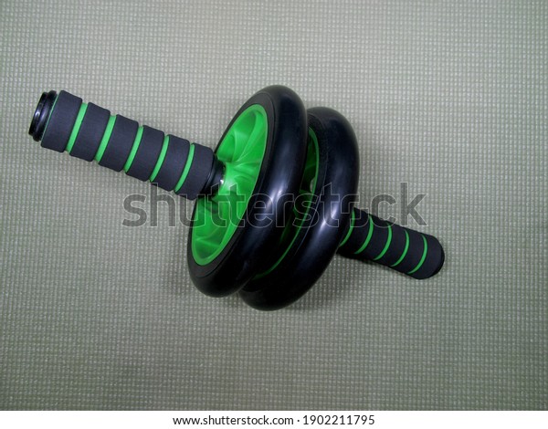 Black and green fitness and roller\
wheel or pumping abs and other muscles on the training\
mat.