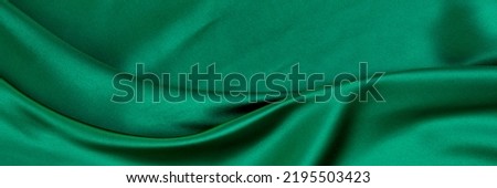 Black green satin dark fabric texture luxurious shiny that is abstract silk cloth background with patterns soft waves blur beautiful.