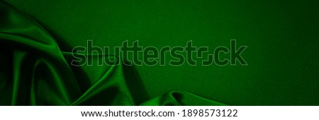  Black green silk satin background. Copy space for text or product. Wavy soft folds on shiny fabric. Top view.Luxurious dark green background. Christmas. Anniversary. Black Friday. Web banner.        