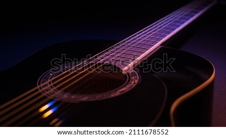 black guitar on a dark background under beam of colored light with copy space. guitar music low-key concept
