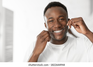 Black Guy Flossing Teeth In The Morning Standing In Bathroom Indoors, Looking At Camera. Healthy Oral Toothcare Hygiene Routine, Cleaning With Floss And Perfect Smile Concept. Free Space For Text - Powered by Shutterstock