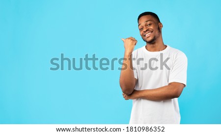 Black Guy Pointing Thumb Aside At Blank Space For Text Standing On Blue Studio Background. Look There Concept. Panorama