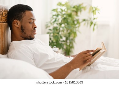 Black Guy Reading Book Lying In Comfortable Bed In Bedroom At Home. African American Man Enjoying Longread Fiction Bestseller Novel Relaxing On Weekend Morning. Read More Concept - Powered by Shutterstock