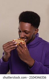 A Black Guy With Short Curly Dark Hair Eating Cheesy Pizza Standing On A Bright Background