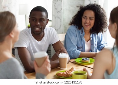 Black Guy Sitting At Table Surrounded By Diverse Multi-ethnic Young Girls. Different Multiracial Students Enjoying Conversation Spending Free Time Together Drinking Coffee Eating Pastries In Cafe