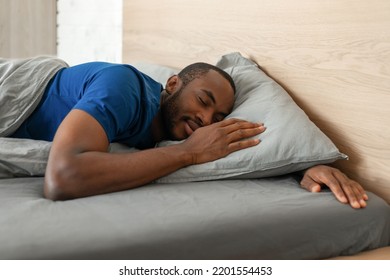 Black Guy Sleeping Peacefully Holding Hands Near Face Lying In Cozy Bed In Modern Bedroom At Home. Millennial Male Napping Resting At Night. Sweet Dreams Concept