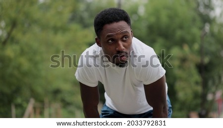 The black guy stopped after jogging in the forest park tired exhausted decided to rest after training. Tired afro american male athlete keeping his hands on knees to normalise breathing after