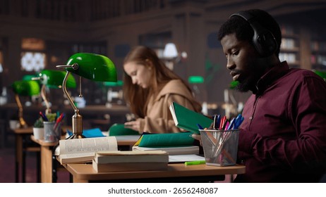 Black guy using study music to help with deep focus for academic success, consulting the campus university database to find reliable sources. Male college student fights for diploma. Camera A.