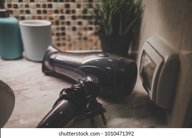 A black hair dryer left near the conventional wall outlet in bathroom