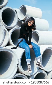 Black hair girl in sweater and jeans chill out on big concrete tube in quiet place.