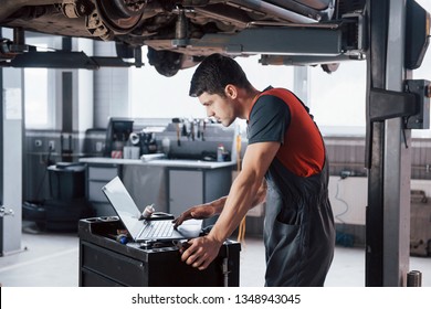 Black hair. Man at the workshop in uniform using laptop for his job for fixing broken car. - Powered by Shutterstock