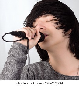 Black Hair Young Guy In Emo Style Is Singing In Microphone On White Background.