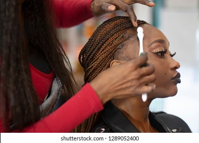 A black hairstylist combing with a toothbrush a beautiful black model.