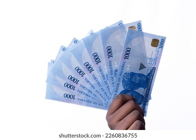 A black hand holding a spread of the New Nigerian currency, money, the 1000 Naira note on a white background - Shutterstock ID 2260836755