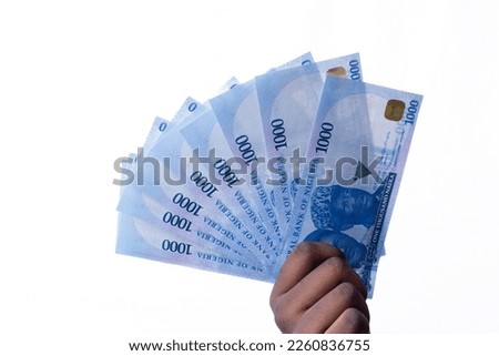 A black hand holding a spread of the New Nigerian currency, money, the 1000 Naira note on a white background