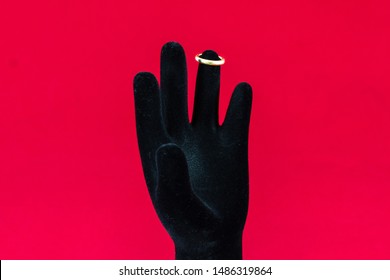 Black Hand With Too Small Golden Ring On Red Background