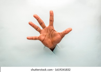 Black Hand Through A Hole In A Cardboard With Open Palm Spread Out Showing All Five Fingers