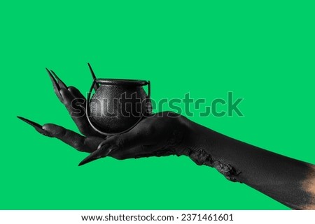 Black hand of witch with cauldron on green background. Halloween celebration