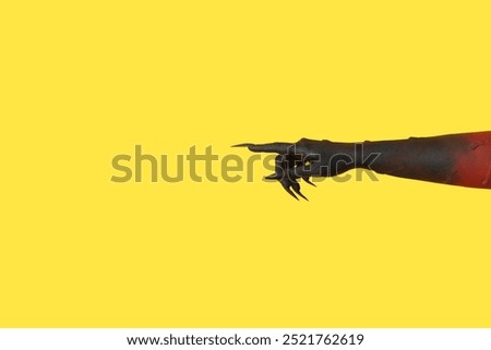 Black hand of witch pointing at something on yellow background. Halloween celebration